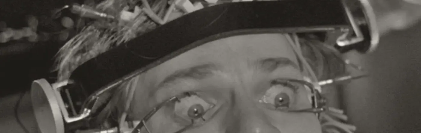 Film still: a man’s eyes held open by clamps