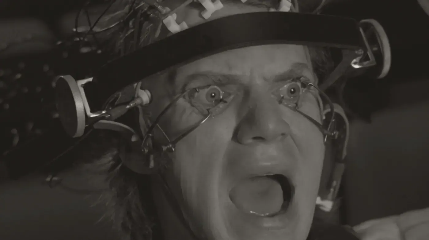 Film still: a man screaming, his eyes held open by clamps